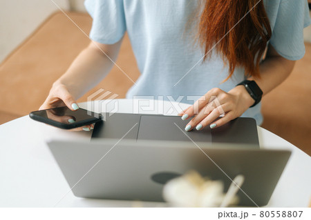 Close-up front view of unrecognizable young woman in smart watch using laptop and phone sitting at table in cafe with warm daylight, selective focus. Close-up front view of unrecognizable young woman in smart watch using laptop and phone sitting at table in cafe with warm daylight, selective focus. 80558807