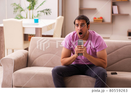 Young man watching tv at home during pandemic 80559263