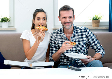 Couple watching TV while eating pizza 80560936