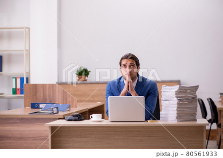 Young male employee unhappy with excessive work in the office Young male employee unhappy with excessive work in the office 80561933