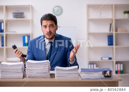 Young male employee unhappy with excessive work in the office Young male employee unhappy with excessive work in the office 80562884