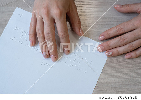 Close-up woman reads the text to the blind. Woman's hands on paper with braille code. Close-up woman reads the text to the blind. Woman's hands on paper with braille code. 80563829