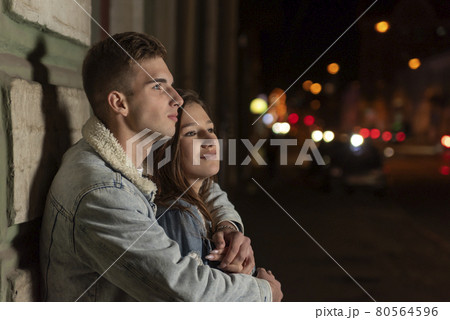 Young guy hugs his beloved on night city background. Beautiful young couple on evening romantic date Young guy hugs his beloved on night city background. Beautiful young couple on evening romantic date 80564596