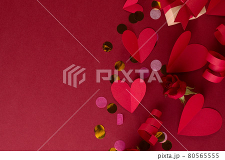 Red paper Hearts, festive decor, and confetti on a dark red background. Valentines Day monochrome border with empty space for text . Red paper Hearts, festive decor, and confetti on a dark red background. Valentines Day monochrome border with empty space for text . 80565555