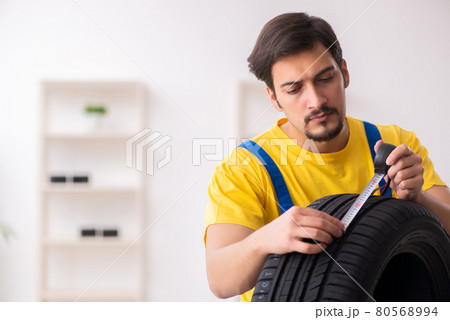Young male garage worker with tyre at workshop 80568994