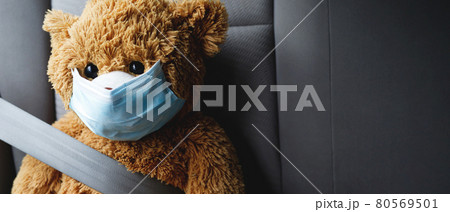A brown teddy bear wearing a mask sits in the car. A brown teddy bear wearing a mask sits in the car. 80569501