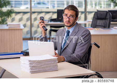 Young male employee in wheel-chair working in the office Young male employee in wheel-chair working in the office 80569748