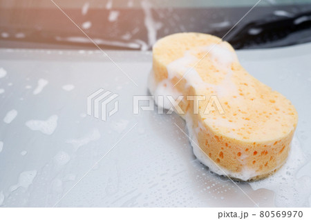Yellow sponge and soap over the car for washing. Motor hood being cleaned. Concept car wash clean. Leave space for writing messages. Yellow sponge and soap over the car for washing. Motor hood being cleaned. Concept car wash clean. Leave space for writing messages. 80569970