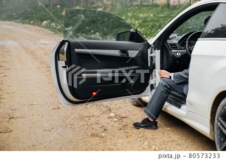 a man sits behind the wheel of a car with the door open and smokes a cigarette. a man sits behind the wheel of a car with the door open and smokes a cigarette. 80573233