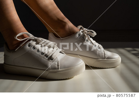 Close-up of female legs in white leather sneakers. 80575587