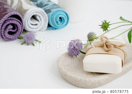 Organic soap bar wrapped in craft paper and tied up with rope lays on tray, different colored towel rolls on background 80578775