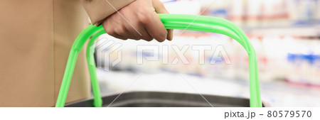 Female hand holds grocery basket on background of store Female hand holds grocery basket on background of store 80579570