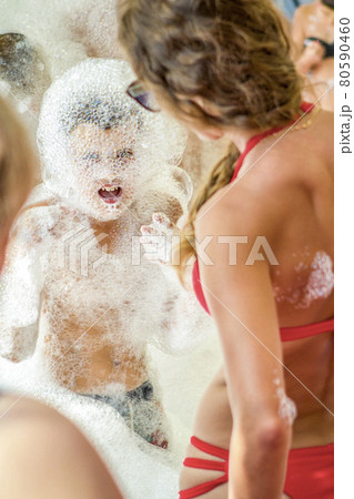 Young boy at the foam party. The face and body are covered with foam. Holiday concept. Young boy at the foam party. The face and body are covered with foam. Holiday concept. 80590460