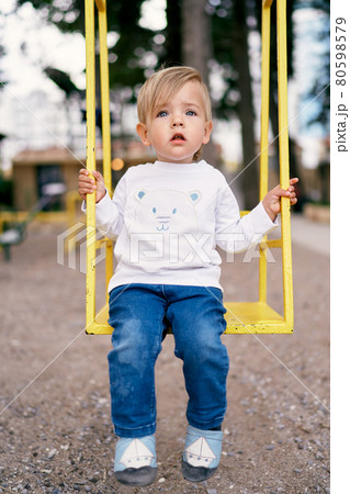 Child sits on a yellow swing in the playground 80598579