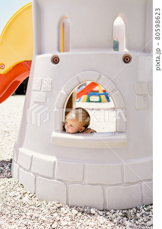 Little girl looks out of the window of a toy fortress on the playground Little girl looks out of the window of a toy fortress on the playground 80598623