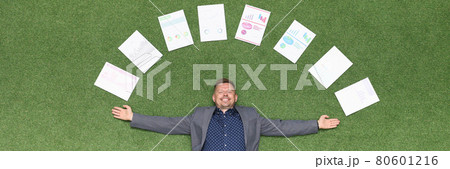 Happy businessman lies on green lawn in documents with business charts Happy businessman lies on green lawn in documents with business charts 80601216