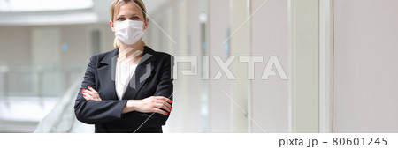 Businesswoman in medical protective mask stands with folded arms in hotel corridor Businesswoman in medical protective mask stands with folded arms in hotel corridor 80601245