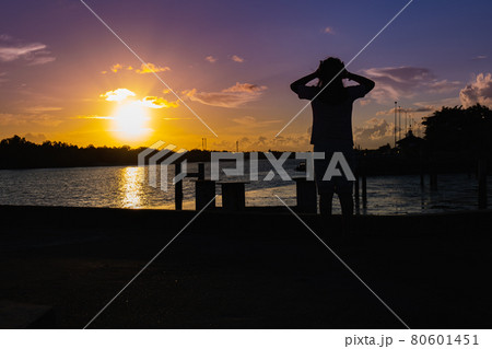 A woman stands at the pier watching the sunset, her figure in the shadows. A woman stands at the pier watching the sunset, her figure in the shadows. 80601451