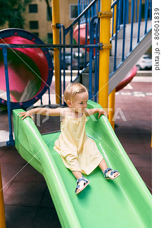 Little girl in a dress slides down a slide on the playground 80601839