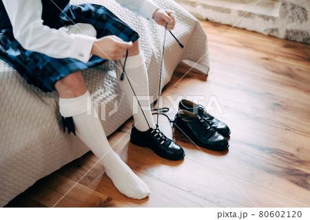 Preparing for a Scottish wedding. Man in a kilt, sporran and high socks sits on the bed and tie long shoelaces on his shoes Preparing for a Scottish wedding. Man in a kilt, sporran and high socks sits on the bed and tie long shoelaces on his shoes 80602120