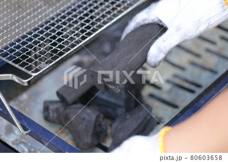 バーベキューの準備で木炭をコンロに乗せる女性の手元 80603658