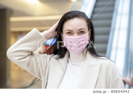 beautiful woman in a pink medical mask on her face against the background of the escadator in a public place beautiful woman in a pink medical mask on her face against the background of the escadator in a public place 80604942