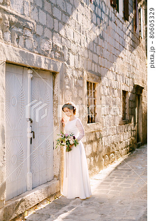 Lovely bride stands near a brick wall. She smiles and holds in her hands a bouquet of beautiful flowers Lovely bride stands near a brick wall. She smiles and holds in her hands a bouquet of beautiful flowers 80605329