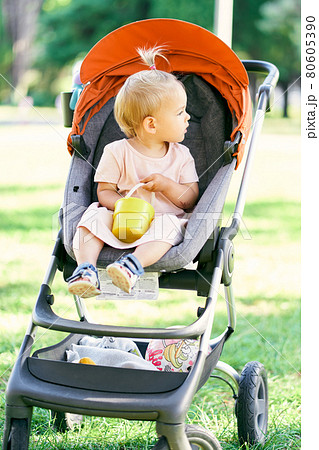 Little girl sits in a stroller in the park and looks away 80605390