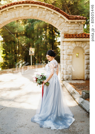 A bride with a wedding bouquet stands under a brick arch at the entrance to the park A bride with a wedding bouquet stands under a brick arch at the entrance to the park 80605446