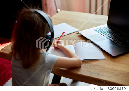 Cute little girl with headphones using laptop to study at home Cute little girl with headphones using laptop to study at home 80606850
