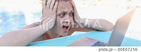 Surprised woman holding her head and looking at laptop screen on side of pool 80607256