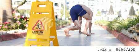 Man falling on tile near sign with inscription caution wet floor closeup 80607259