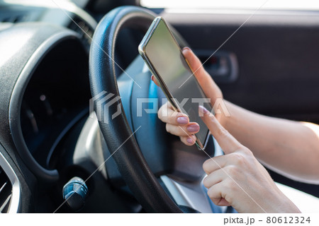 A faceless woman uses a mobile phone while driving a car. The girl uses the navigation in the smartphone 80612324