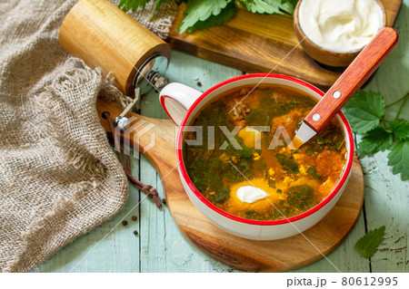 Fresh homemade nettle and meat soup served with sour cream on a rustic table. 80612995