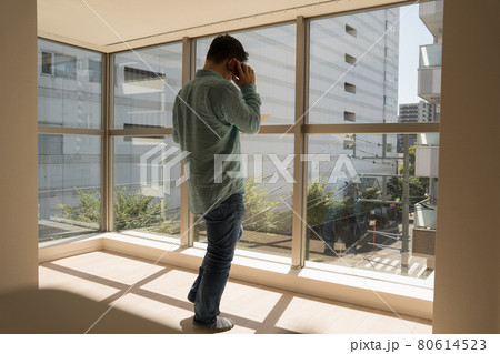 とても日当たりのよい新築マンションのリビングでスマホを使って電話する中年男 80614523