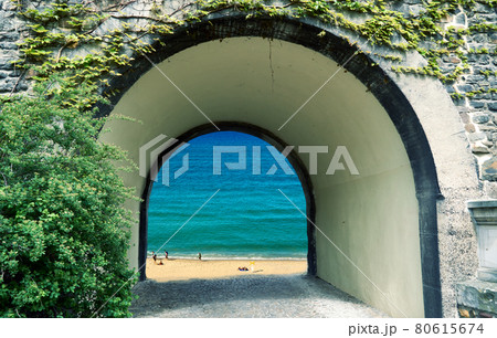 View through an arched gate to a bright beach with unrecognizable people and blue sea, daydream, composition View through an arched gate to a bright beach with unrecognizable people and blue sea, daydream, composition 80615674
