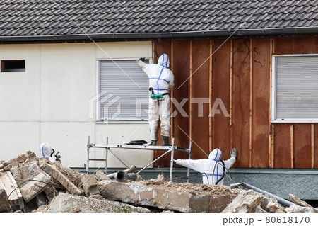 Professionals in protective suits remove asbestos on a wall Professionals in protective suits remove asbestos on a wall 80618170