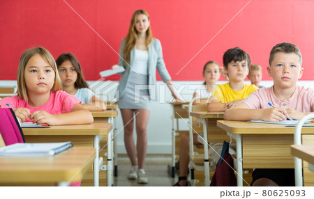 Focused preteen pupils studying in classroom with female teacher Focused preteen pupils studying in classroom with female teacher 80625093