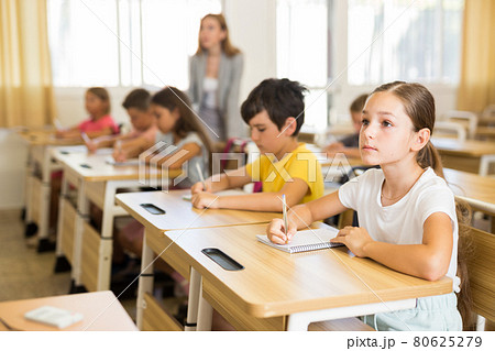 Diligent tween schoolgirl making notes of teacher lecture Diligent tween schoolgirl making notes of teacher lecture 80625279