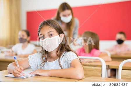 Preteen schoolgirl in protective face mask studying in classroom 80625487