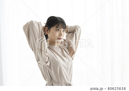 窓際で髪の毛を束ねる若い女性 80625638