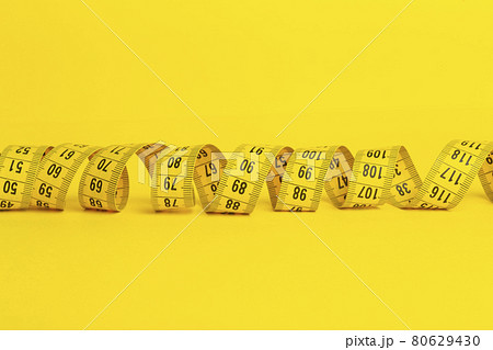 Measuring tape on a yellow background. Measuring tape in the shape of a spiral twisted on a yellow background. Slimming and diet concept, copy space Measuring tape on a yellow background. Measuring tape in the shape of a spiral twisted on a yellow background. Slimming and diet concept, copy space 80629430