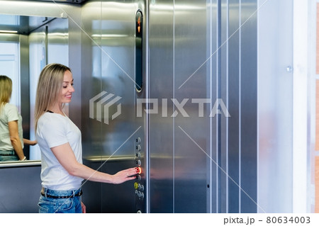 Happy blonde woman pushing elevator button. 80634003