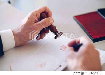 Close-up of a person's hand stamping with approved stamp on certificate or other document. 80634036