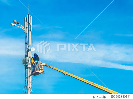 Two men, raised on a crane, will repair the power line support against the blue sky. Dangerous profession, selective focus 80638847