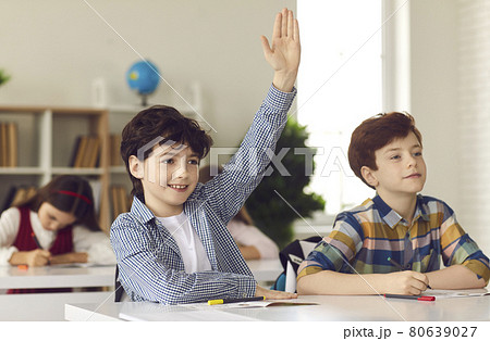Schoolboy sits in a classroom with his hand raised wanting to give the right answer or participate. Schoolboy sits in a classroom with his hand raised wanting to give the right answer or participate. 80639027