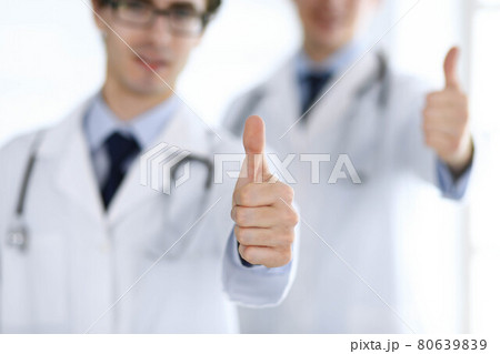 Two male doctors standing as a team and showing thumbs up as a symbol of the best service for patients in the clinic. Medicine and health care 80639839