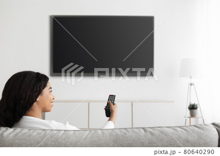 Fun in the evening. Relaxed black lady watching TV pointing remote control at flatscreen television with black screen Fun in the evening. Relaxed black lady watching TV pointing remote control at flatscreen television with black screen 80640290
