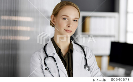 Friendly smiling female doctor standing in clinic. Portrait of friendly physician woman. Perfect medical service in hospital Friendly smiling female doctor standing in clinic. Portrait of friendly physician woman. Perfect medical service in hospital 80640673