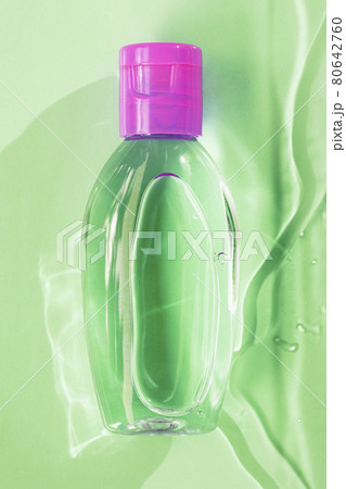 Small green transparent bottle with pink cup, on green background with water, top view 80642760